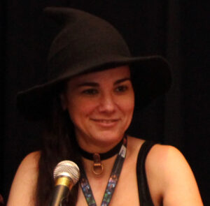 Picture of Jennifer Blackstream on a panel at a convention wearing a witch hat.